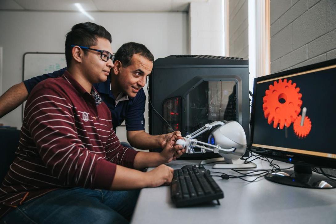 A Kettering professor and student work on a project using haptic technology with results displayed on a computer screen